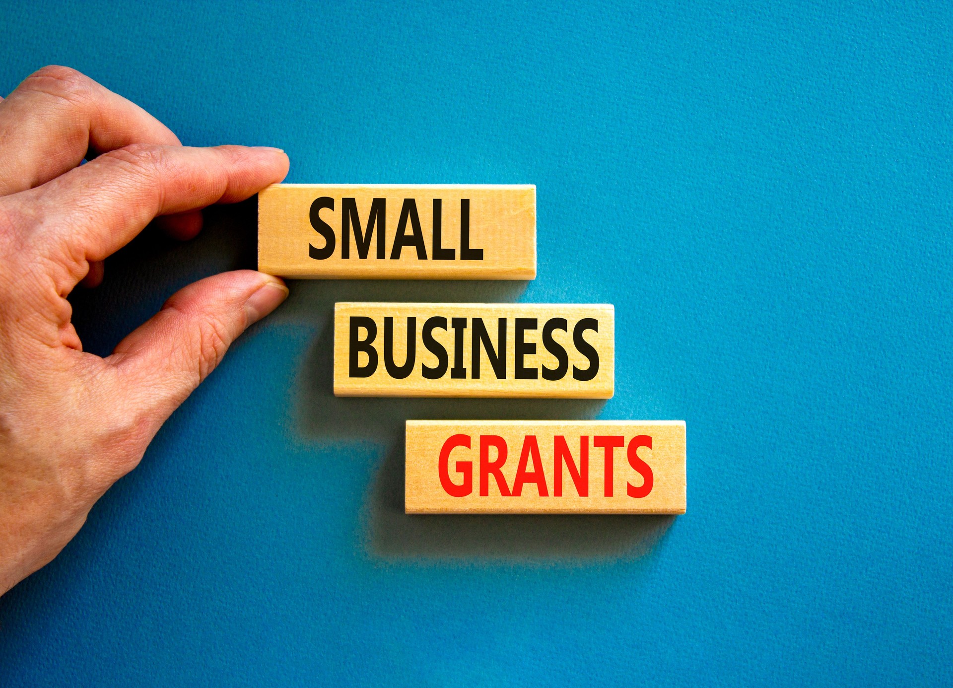 Small business grants symbol. Concept words Small business grants on wooden blocks on a beautiful blue table blue background. Businessman hand. Business, finacial and small business grants concept.