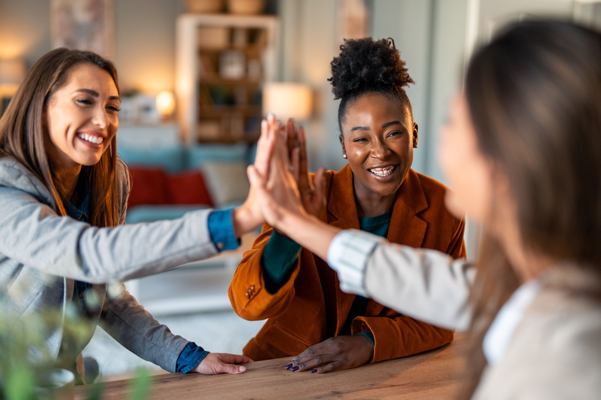 Successful businesswomen united as a team high fiving in an office while sitting at the table