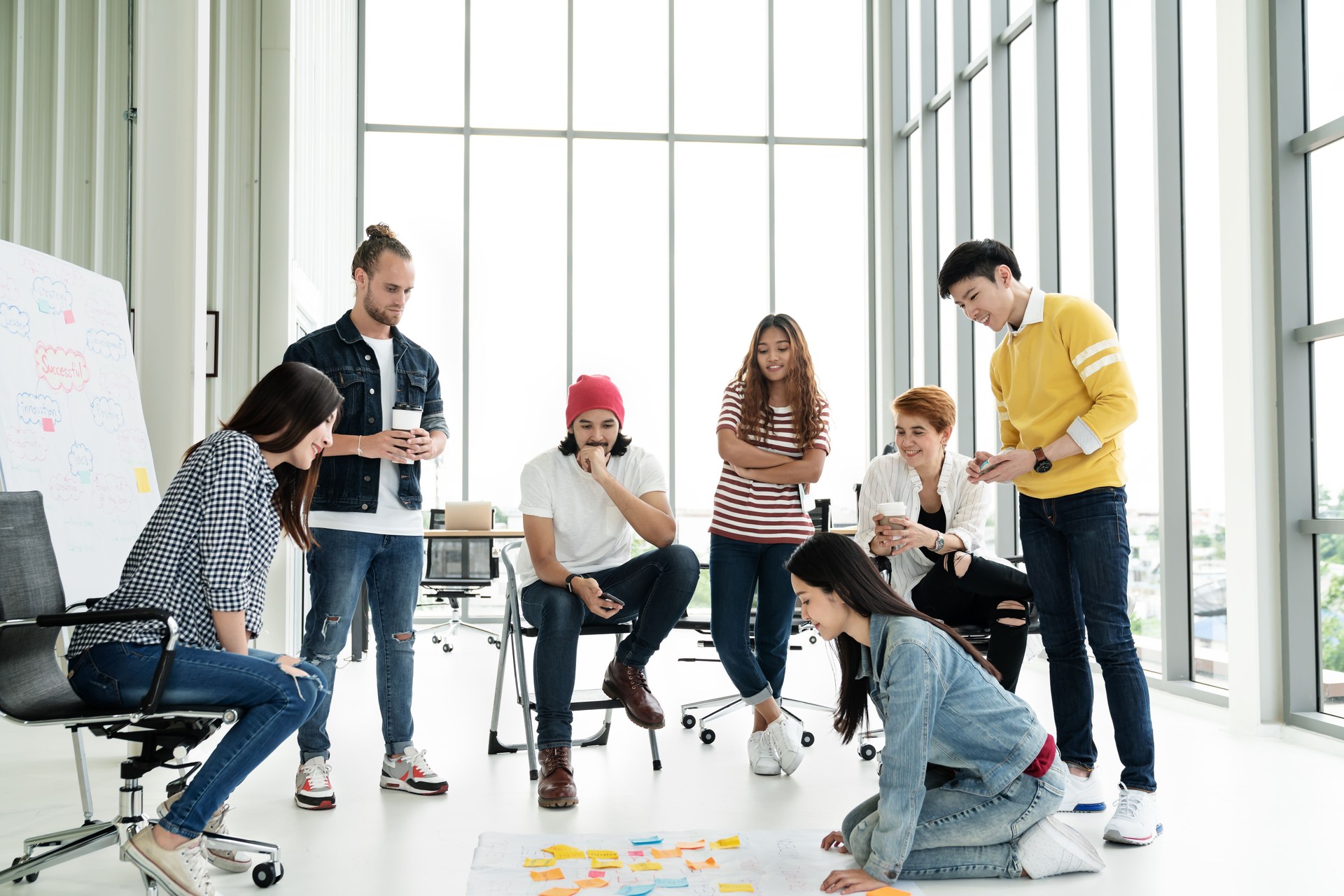 Young creative diverse group meeting and looking at project plan lay out on floor discuss or brainstorm business strategy with post note. Workshop for startup team in modern office. Happy workplace.