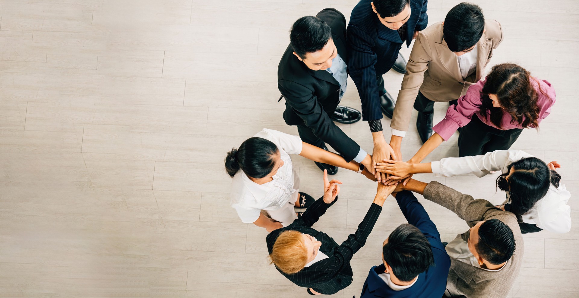 Four businesspeople of diverse backgrounds stand in a circle stacking their hands to represent unity. This image signifies teamwork success and global collaboration.